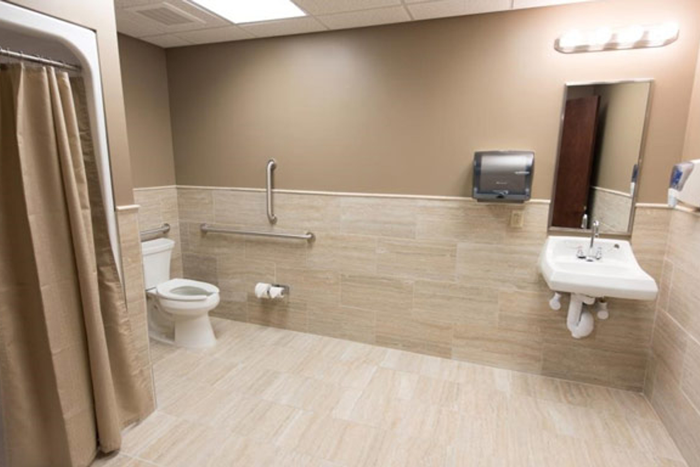 A Tristar Sleep Center bathroom, beige colored, with a toilet, sink, mirror and shower. 
