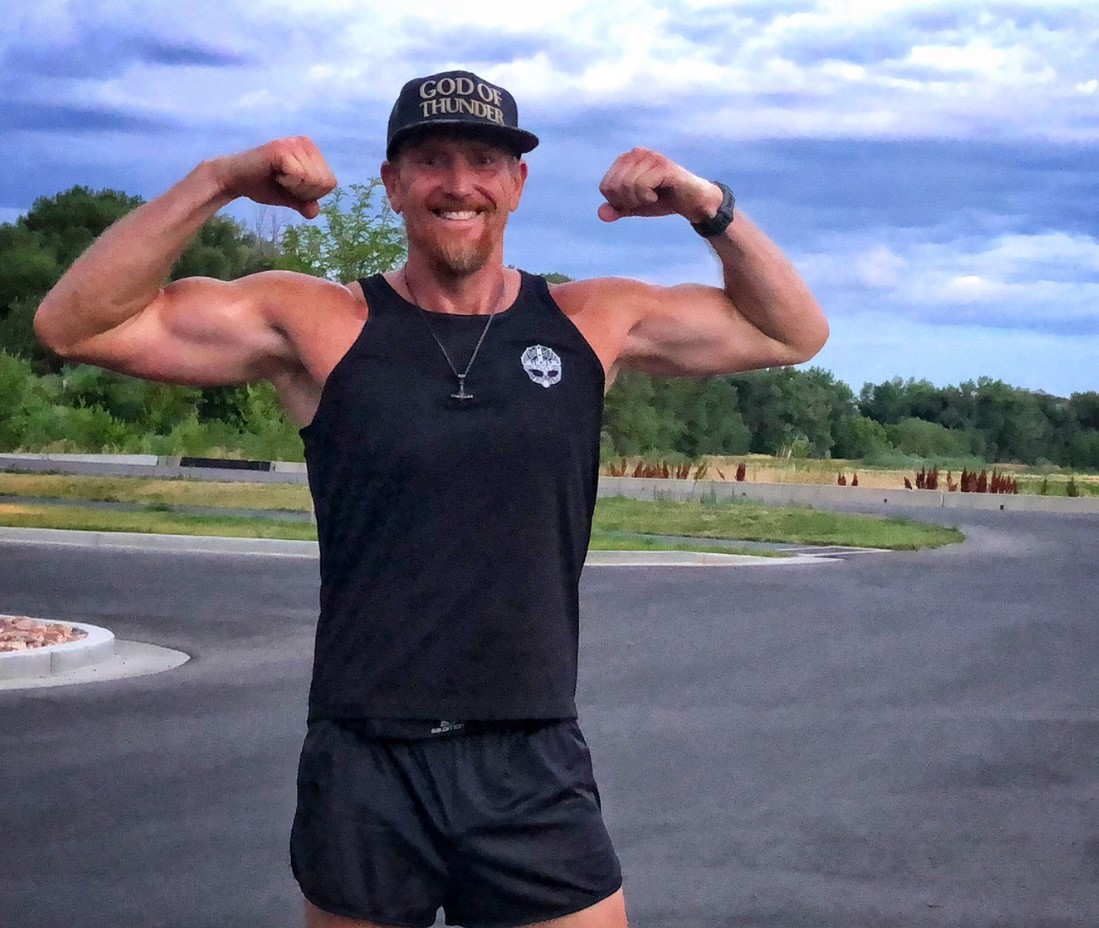 Aaron Jensen flexing his biceps on a paved road.