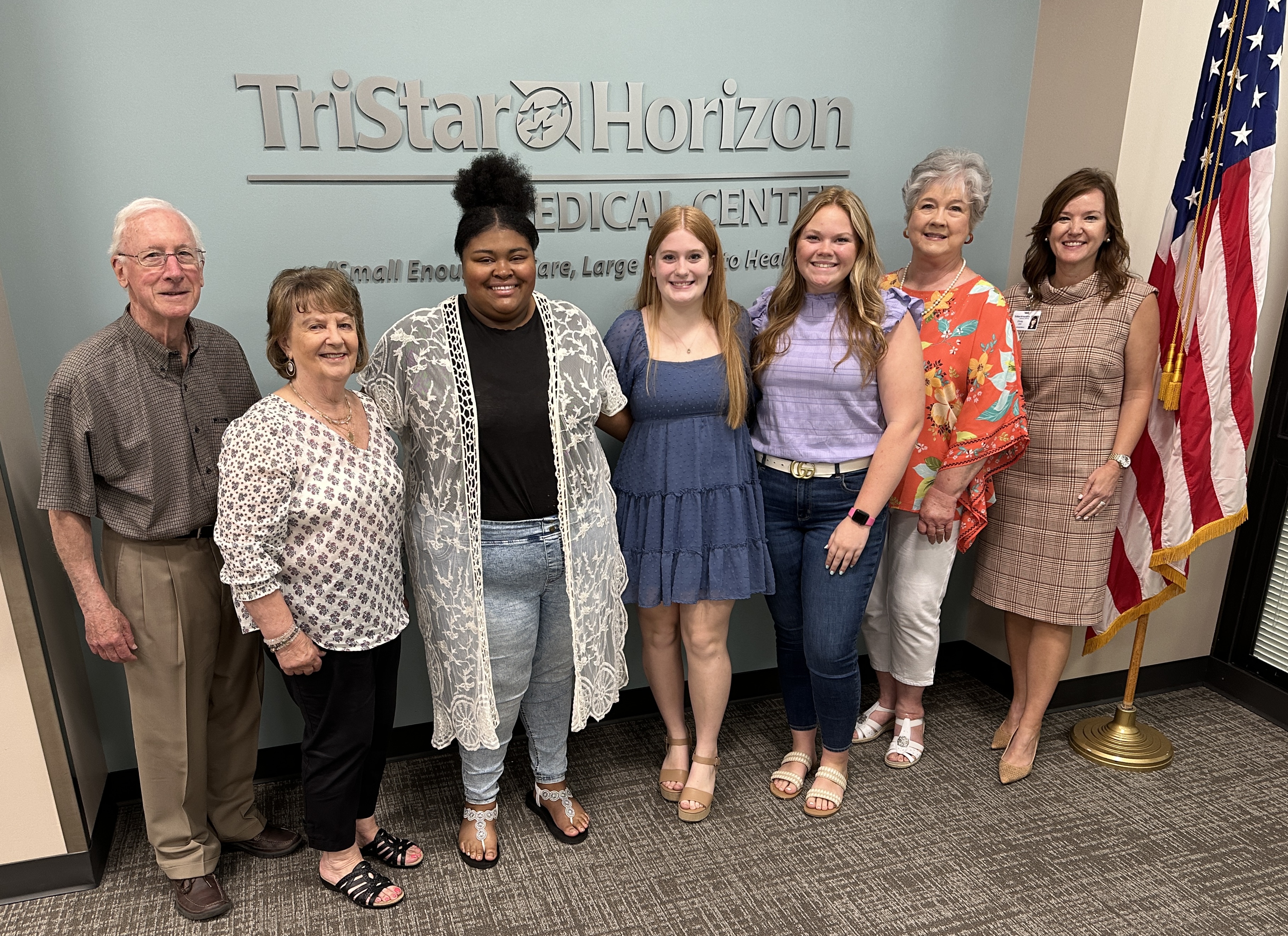 Seven people gather together, including three scholarship recipients, three volunteers and hospital CEO