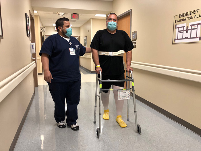 Rolando being assisted by a nurse and a walker in a hospital.