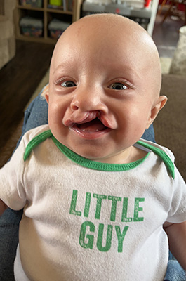 Obadiah Freeman smiles while wearing a onesie that reads, "Little guy."