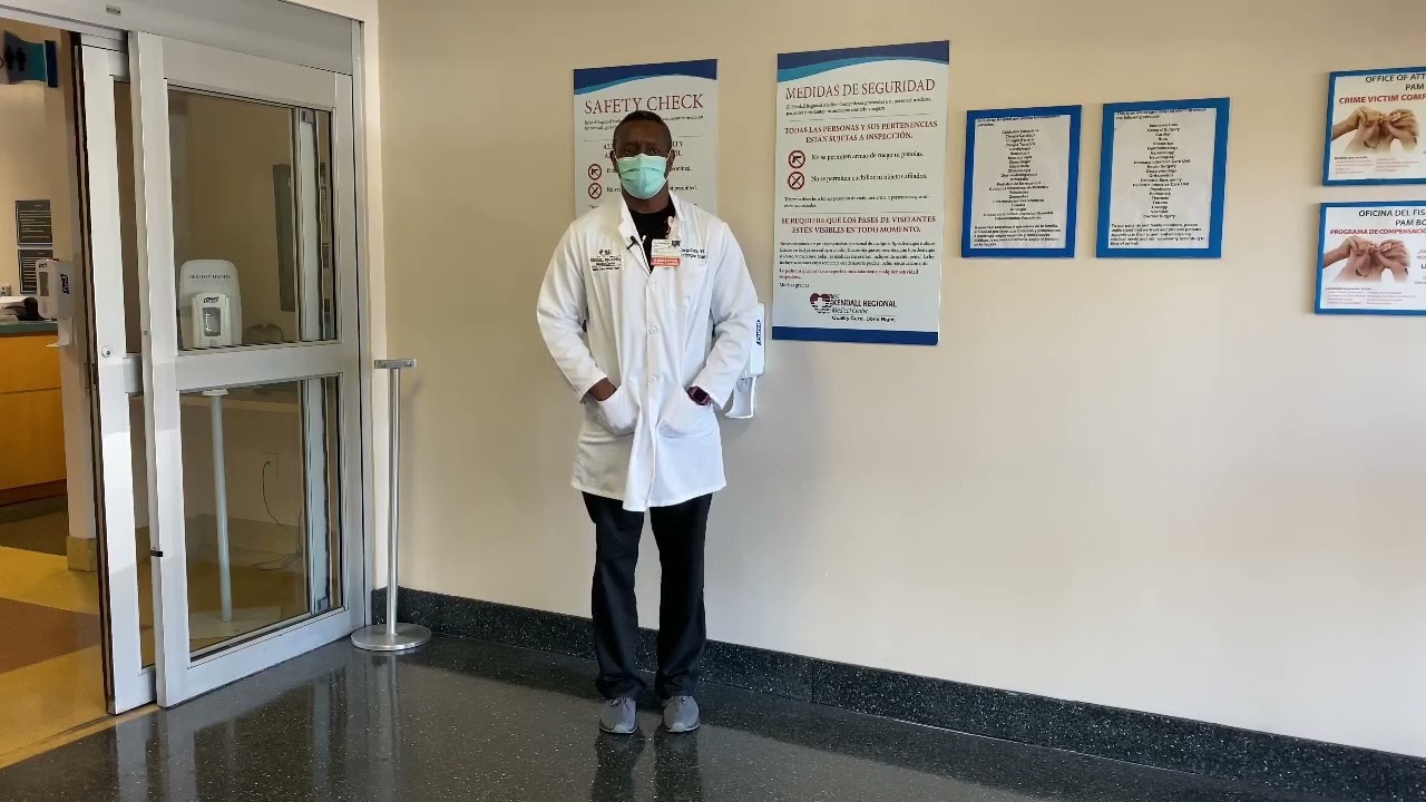 A doctor wearing a mask standing in front of a wall at the entrance of the hospital