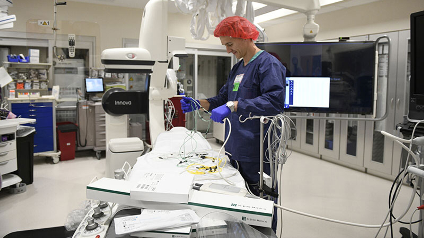A technician working at electrophysiology equipment in a large room.