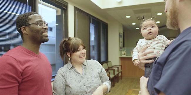 Hristina Nesheva and her husband smiling while a member of the hospital staff holds baby Milena.