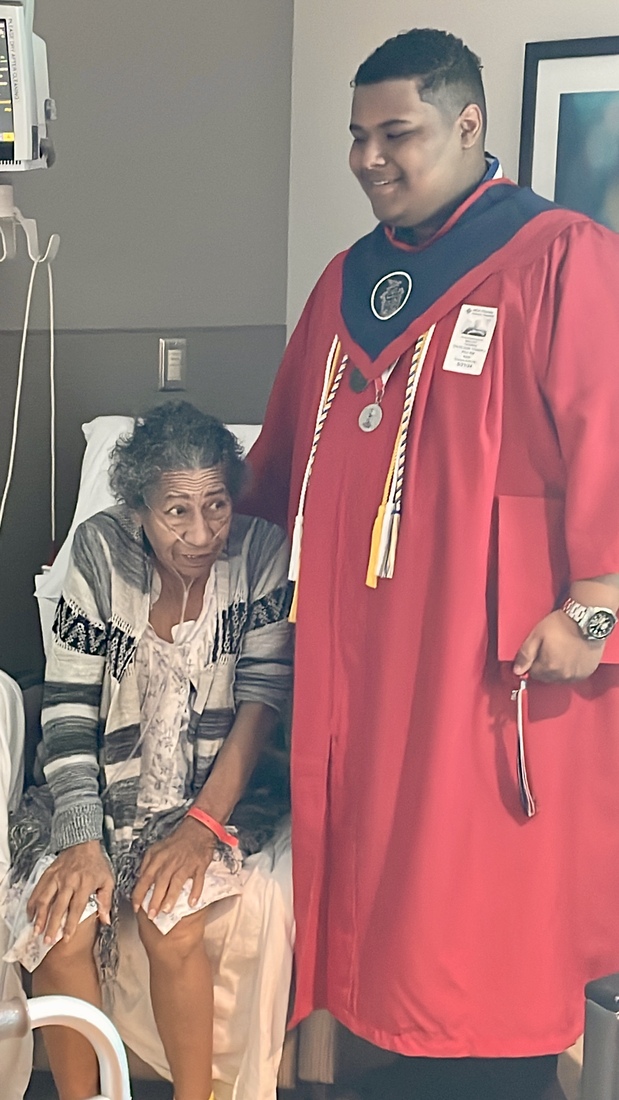 High school graduate in red robe and cap with grandmother at hospital room