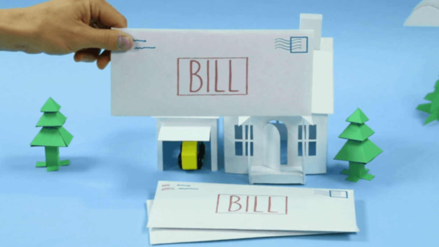 A hand holding an envelope that says "Bill" over a stack of bills with a paper house and trees behind it