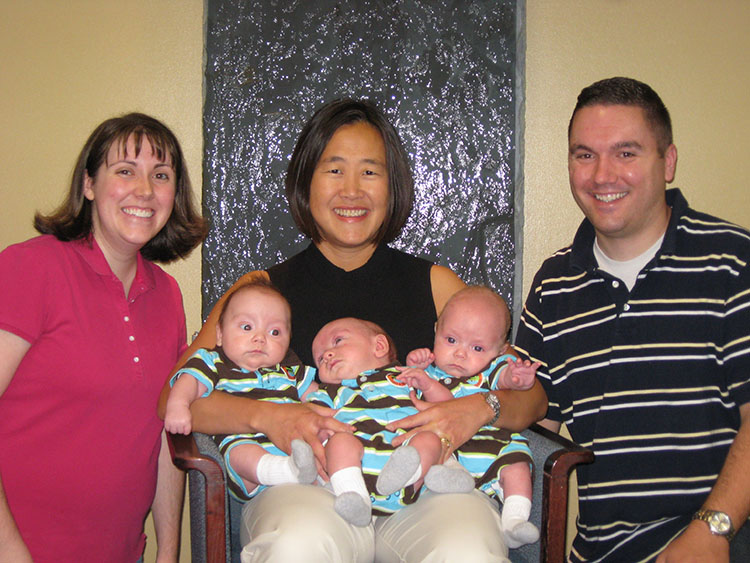 Melissa Hedin and husband Mike pose on each side of a seated Dr. Susan Horvath holding all three Hedin triplets.