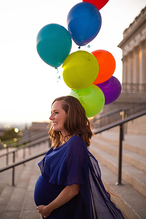 Crystalee Beck turned to her side, smiling and holding her pregnant belly, with balloons beside her.