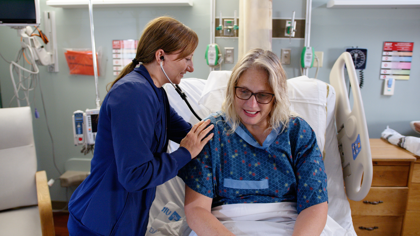 Olga Shunyayev, RN, listening to the lungs of Kimberly Cansler in a hospital room using a stethoscope