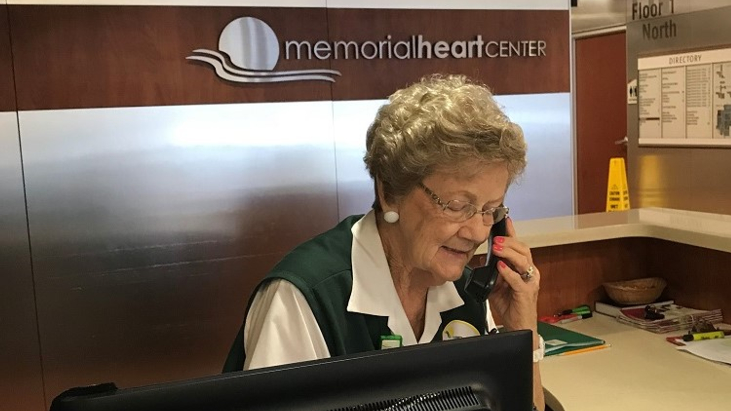 Memorial Hospital volunteer seated at a desk and talking on a phone.