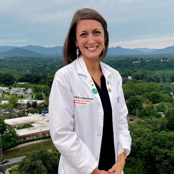 Ashley Hudson smiles while wearing a white lab coat, standing on the roof of the hospital, with the city in the background.
