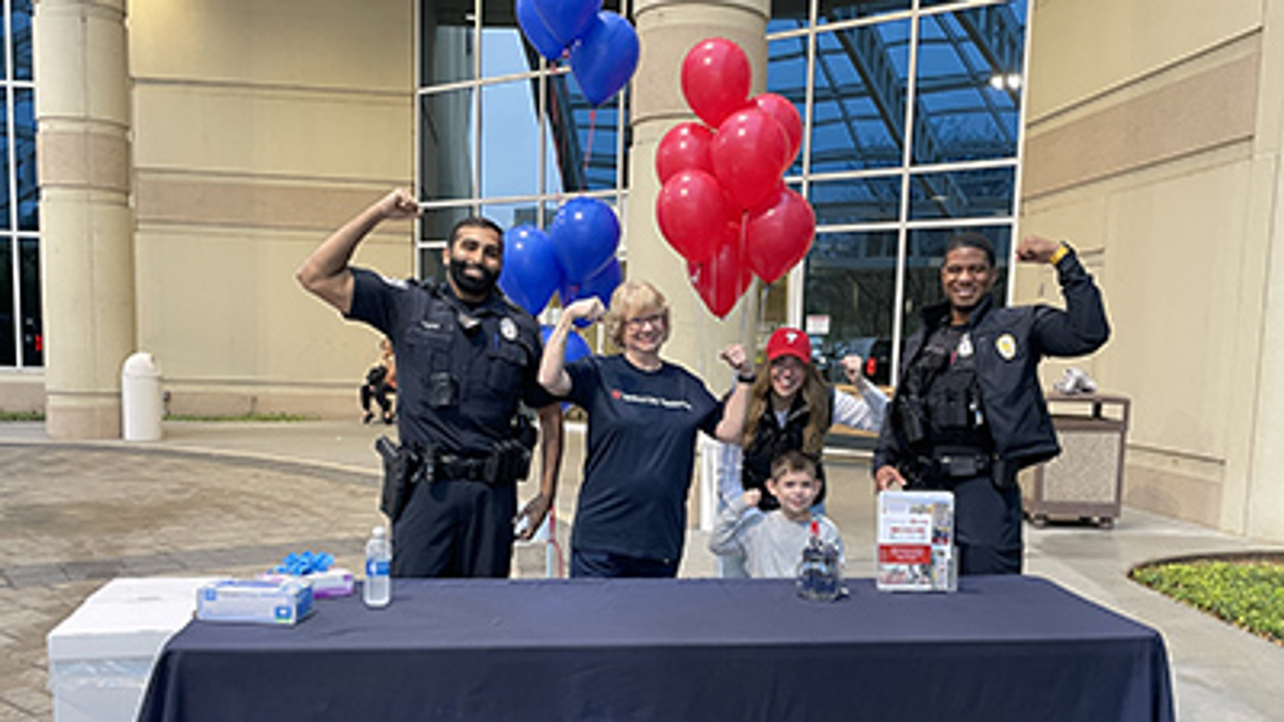 Hospital staff and police officers hold up their arms, flexing their biceps, during a medication donation event.