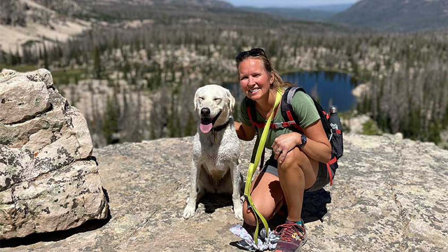 Tara W. poses with her dog on a rocky ledge while hiking.