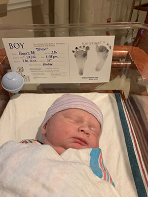 New Years 2022 infant Colton Rogers is sleeping inside a hospital bassinet wrapped in blanket and wearing a beanie.  His feet prints and medical information is seen on a card attached at the head of the bassinet.