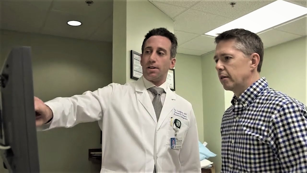 Dr. Eric Schiffman points to a computer monitor while talking to a patient. 