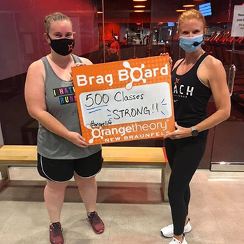 Mackenzie Mitchell and friend holding a sign that says "Brag Board 500 classes strong!".