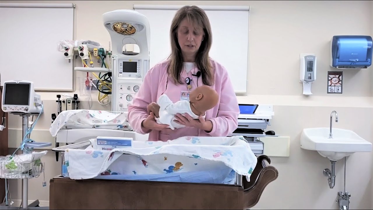 Nurse demonstrating breastfeeding techniques with a mannequin baby.