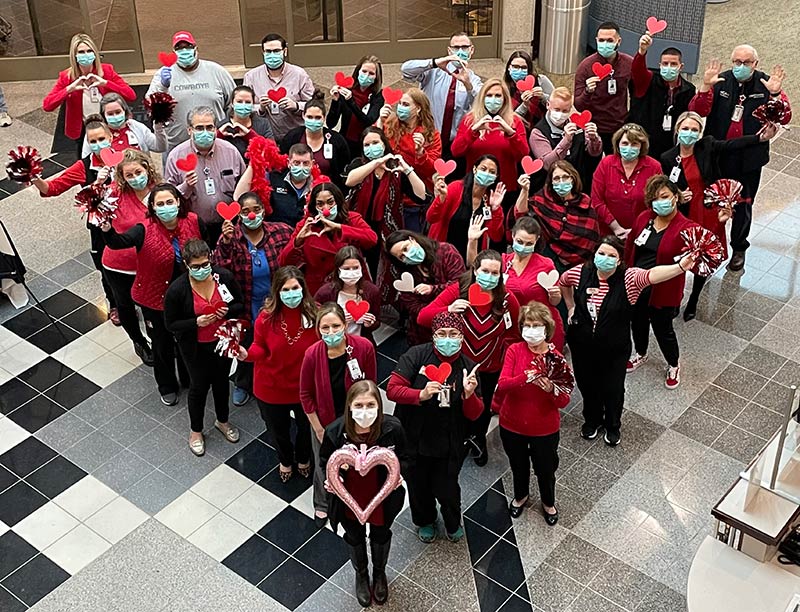From above, a large group of Tristar Summit Medical Center staff members stand in a heart shaped formation while holding heart shaped in the air. They are dressed in red colors in recognition of American Heart Month.