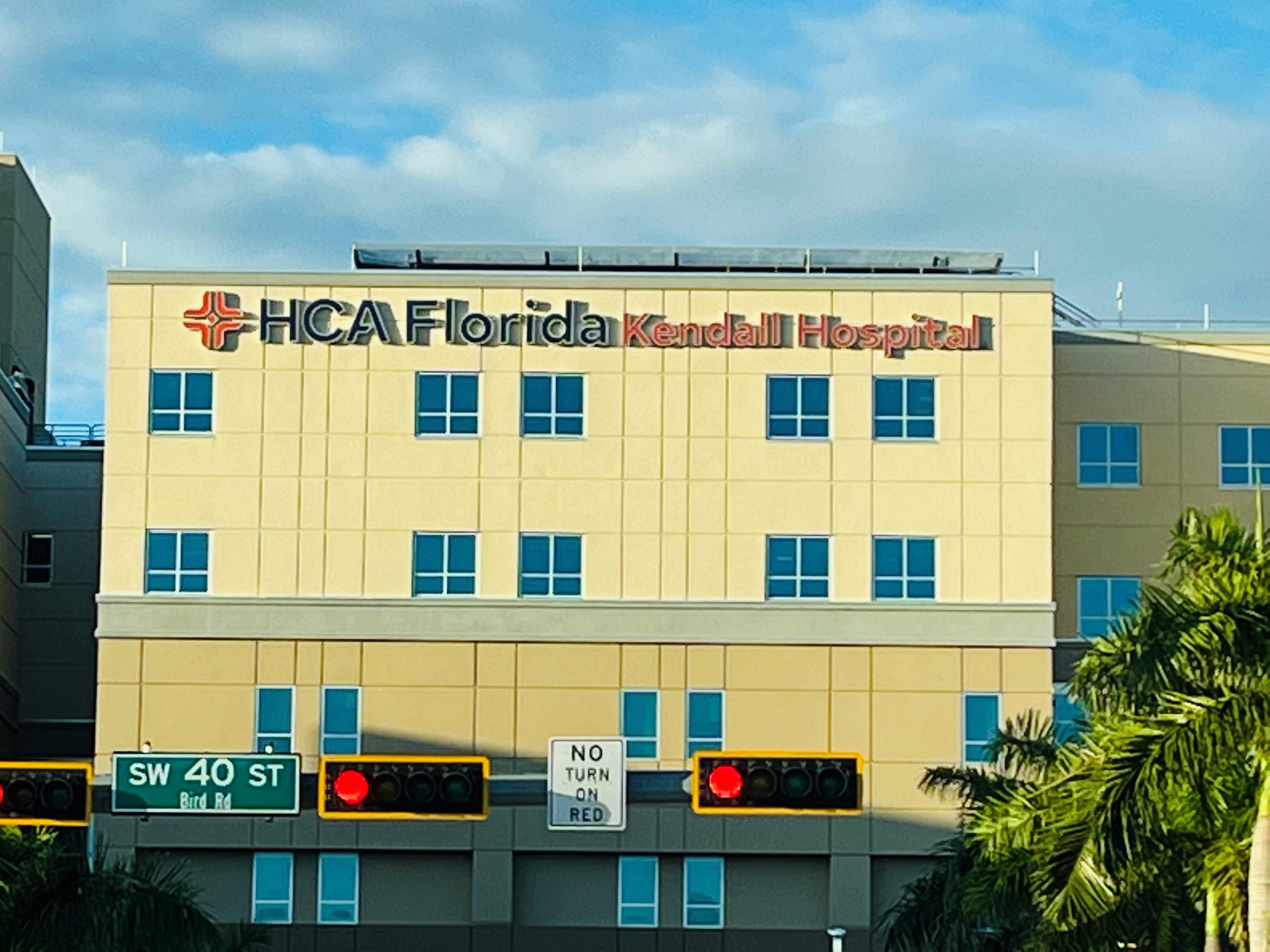 Exterior photo of Kendall Hospital showing sign, palm trees, and traffic lights.