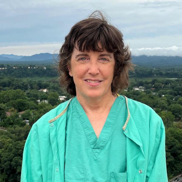 Lisa Clark smiles while wearing green hospital scrubs, standing on the roof of the hospital with the city in the background.