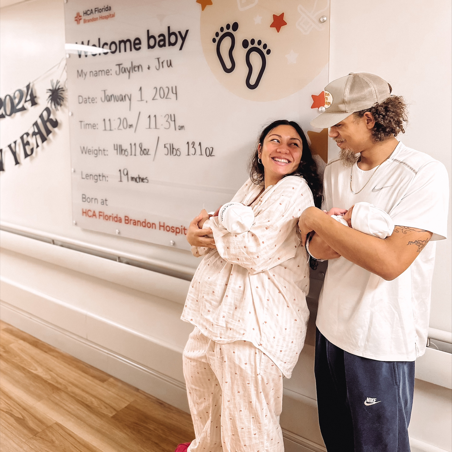 Proud parents of identical twins, Kelsi and Jaylen Pung are holding their baby boys in front of a large birth announcement.