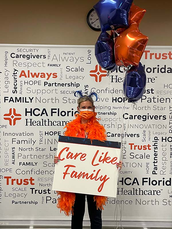 Health care professional holding balloons and a sign saying care like family