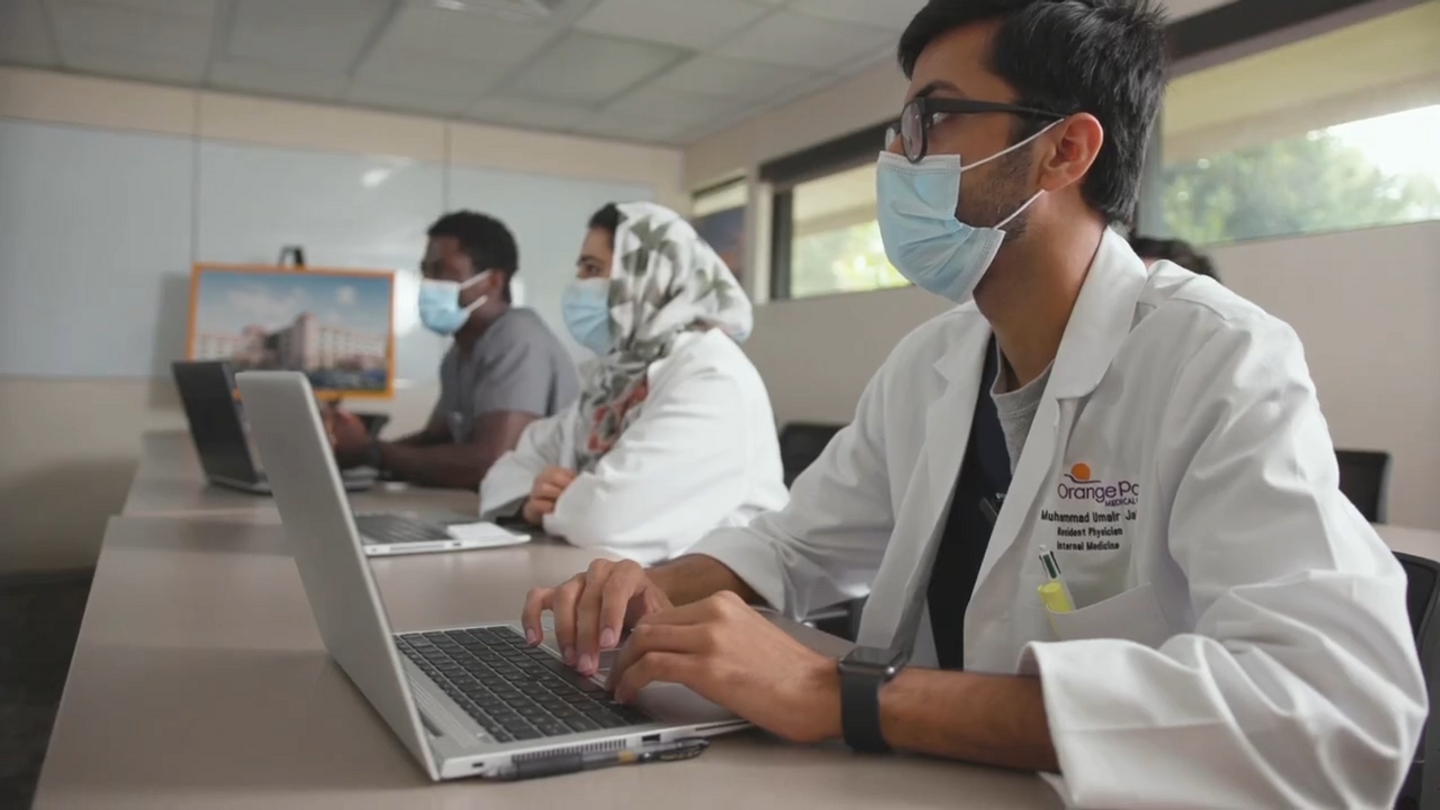 Medical residents sit in a classroom with laptops.