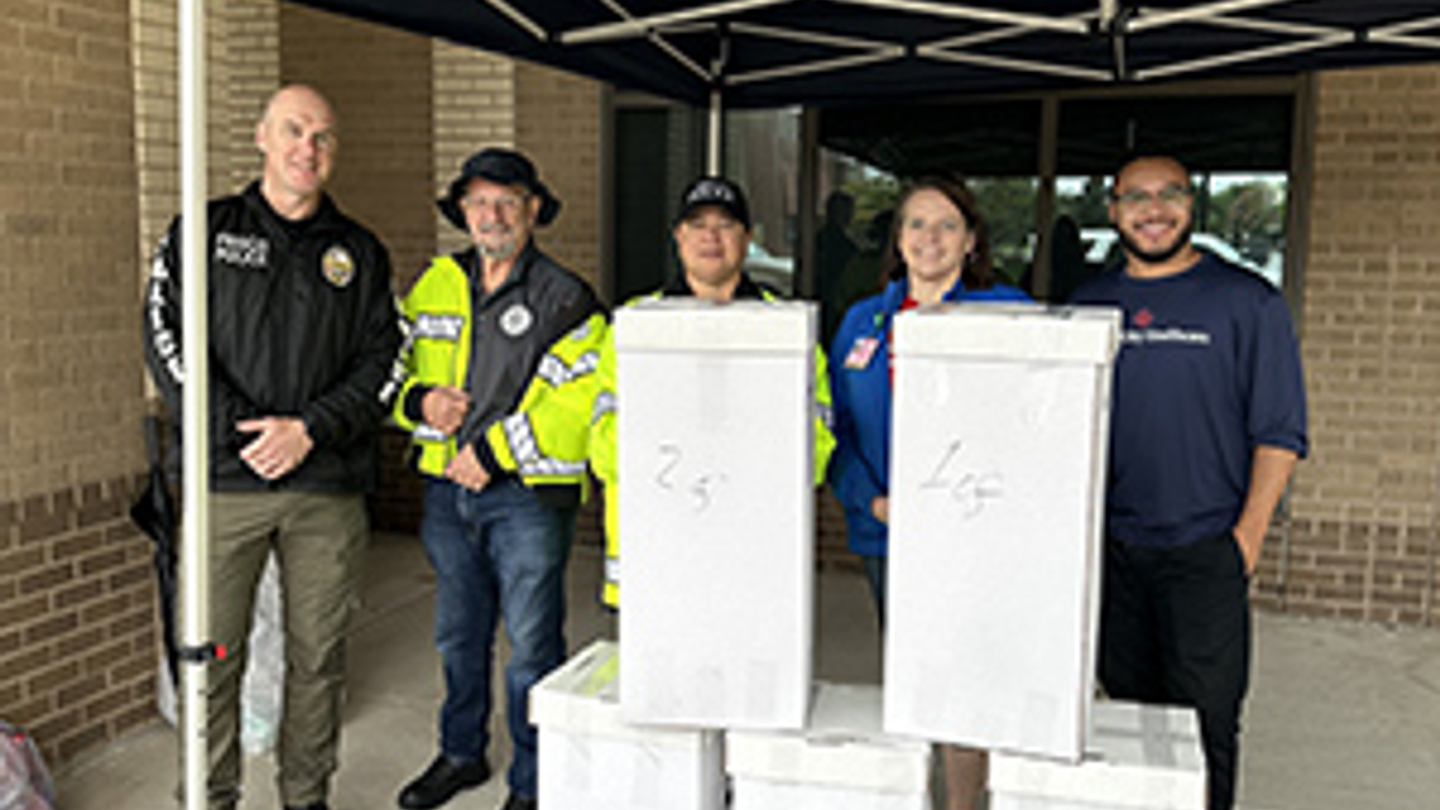 Hospital staff and police officers smile while standing next to medication drop boxes.