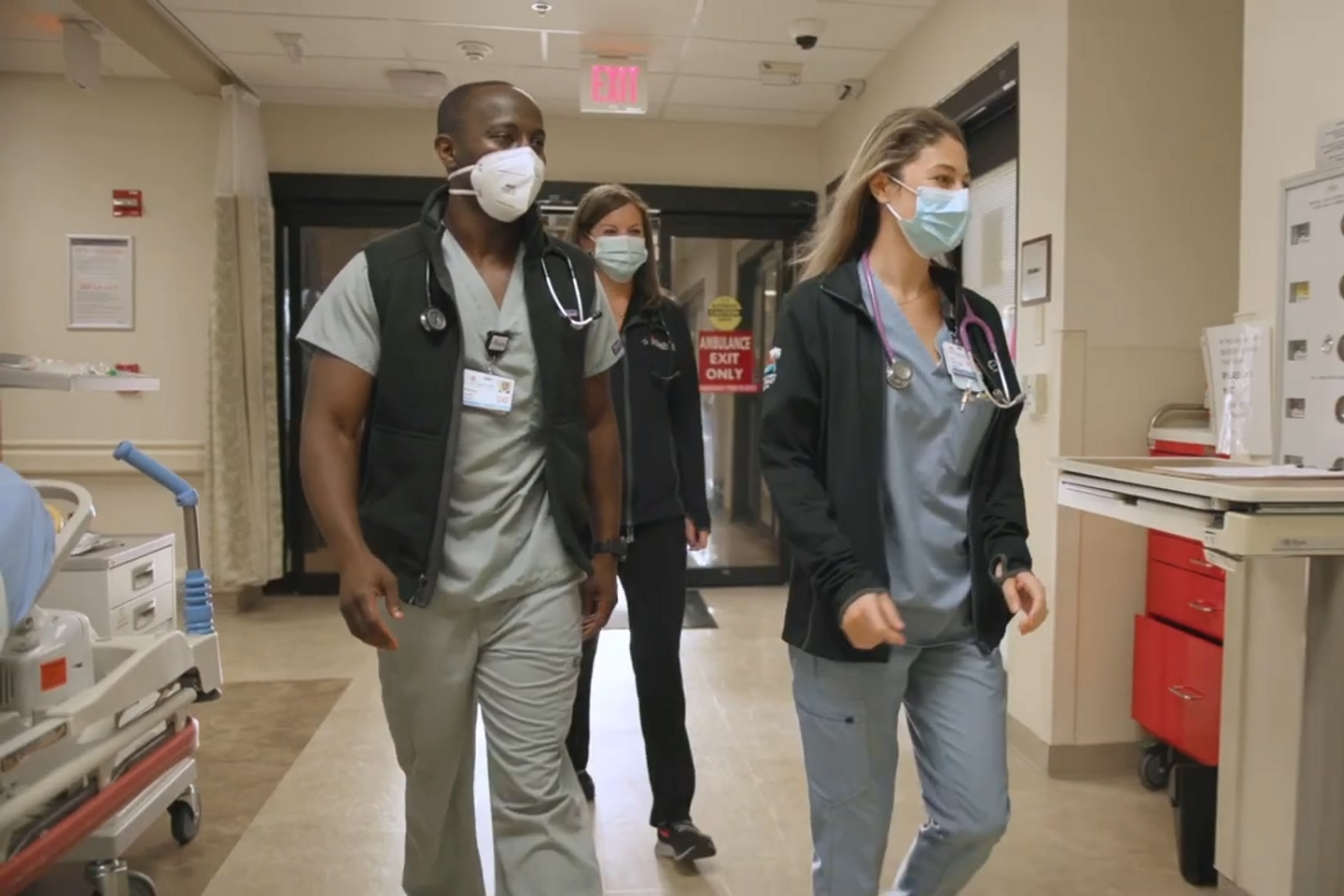 Three emergency care providers walk through a hospital wing.