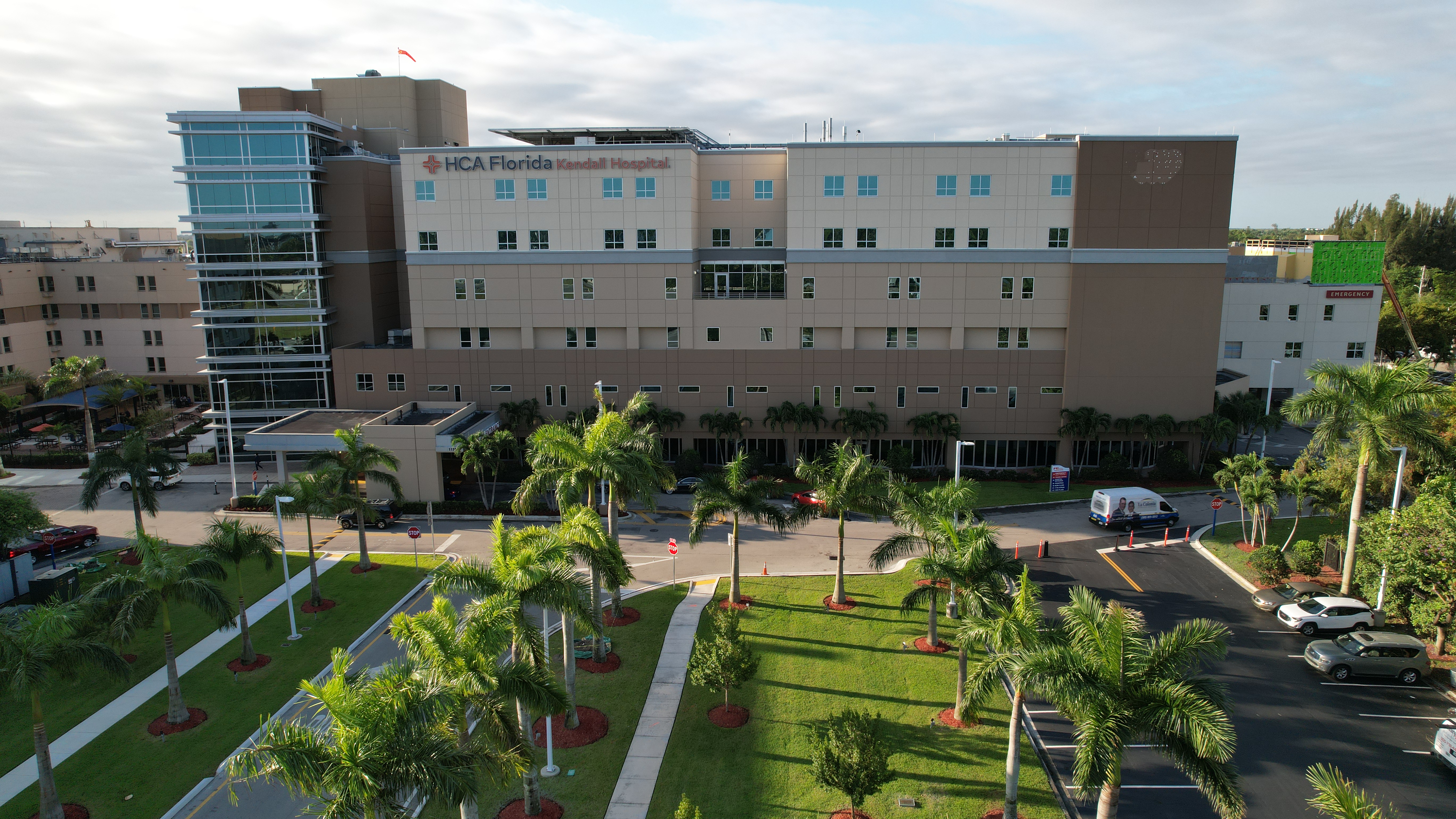 Kendall Hospital entrance, a white, tan, brown building. Walkways ined by palm trees.