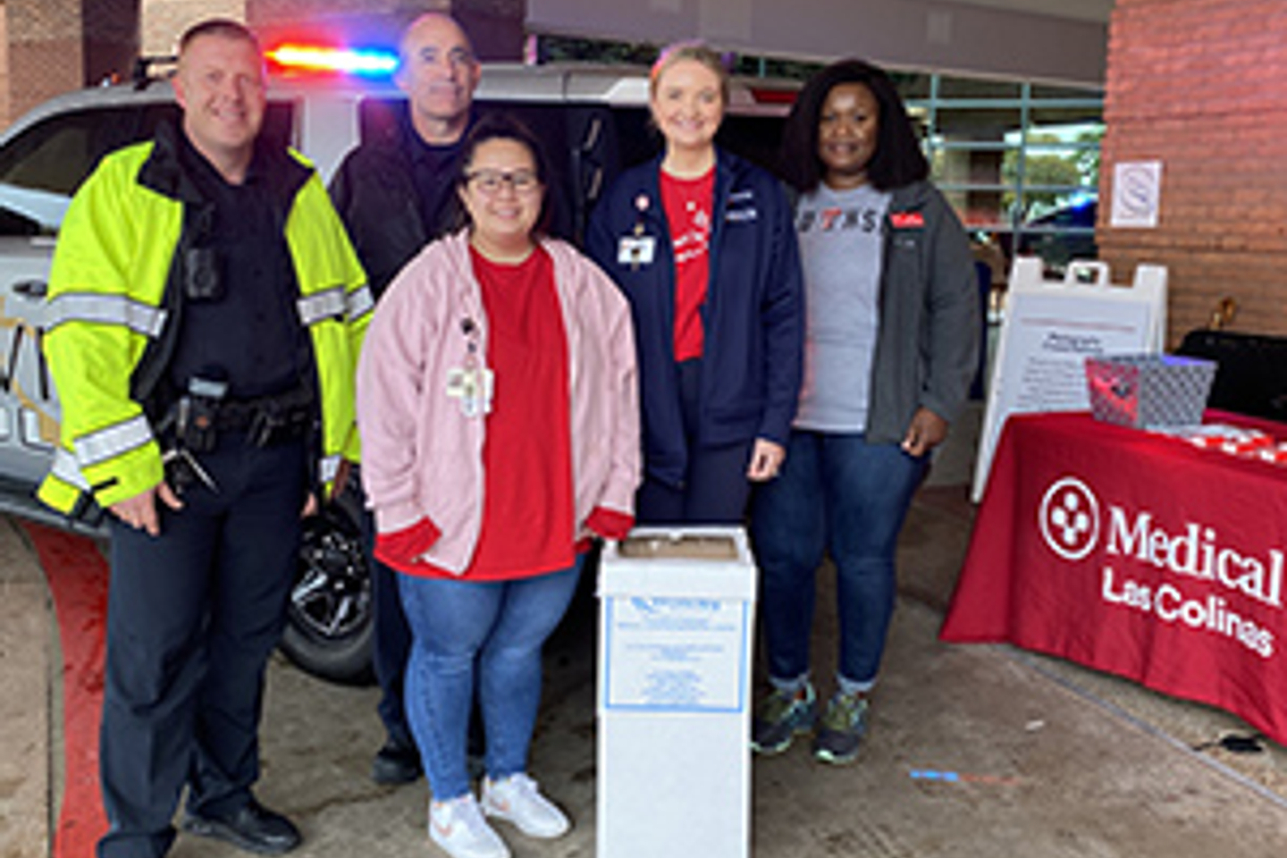 Hospital staff and police officers smile while standing next to a medication drop box.