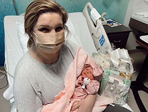 Newborn infant and New Year's Day baby Sophie is wrapped in a pink blanket and is held by her mother who is seated on a hospital bed.