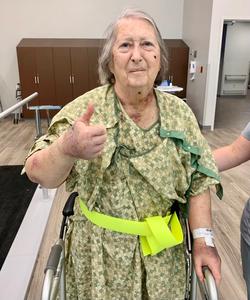 Patsy using a walker in rehab, giving a thumbs up.