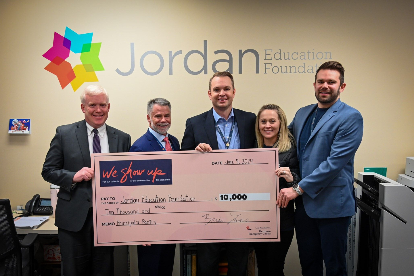 Five individuals from the Jordan Education Foundation and Lone Peak Hospital smiling while holding a giant ceremonial check