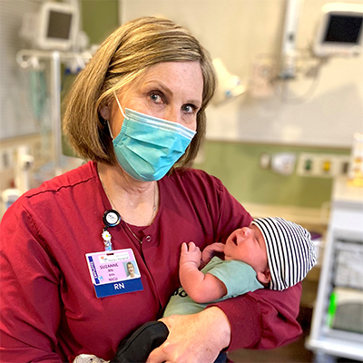 Suzanne Wouden wearing a mask, holding a newborn baby.