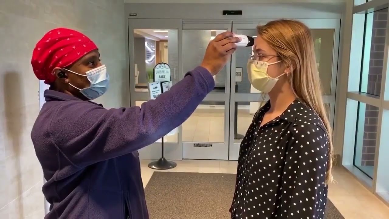 A hospital staff member wearing a mask takes the temperature of a hospital visitor wearing a mask