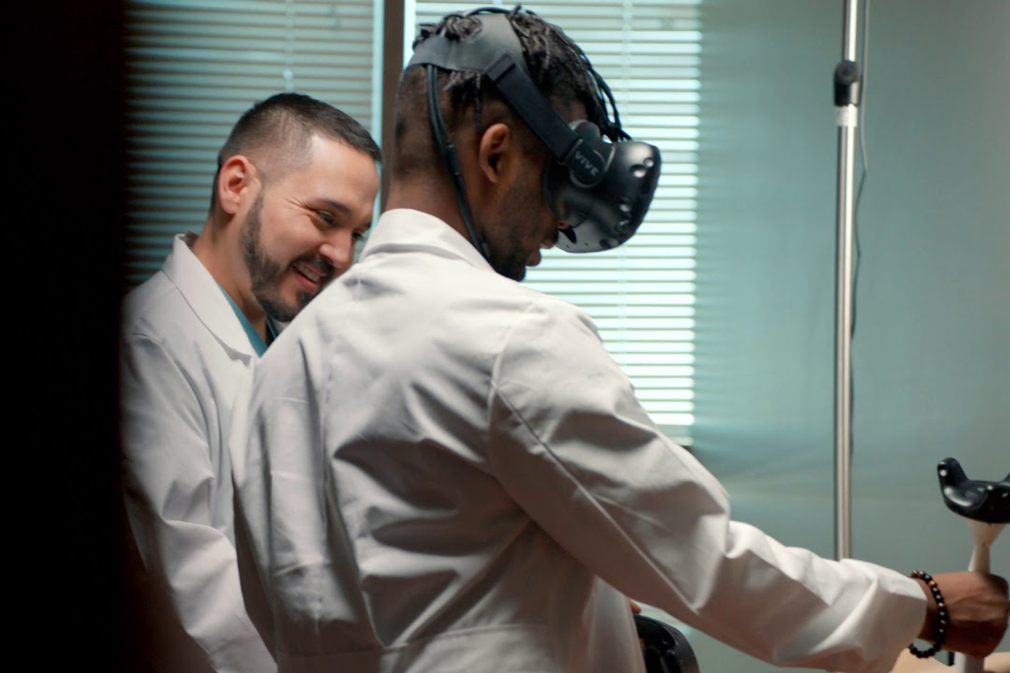 A med student wears a virtual reality headset while a colleague looks on.