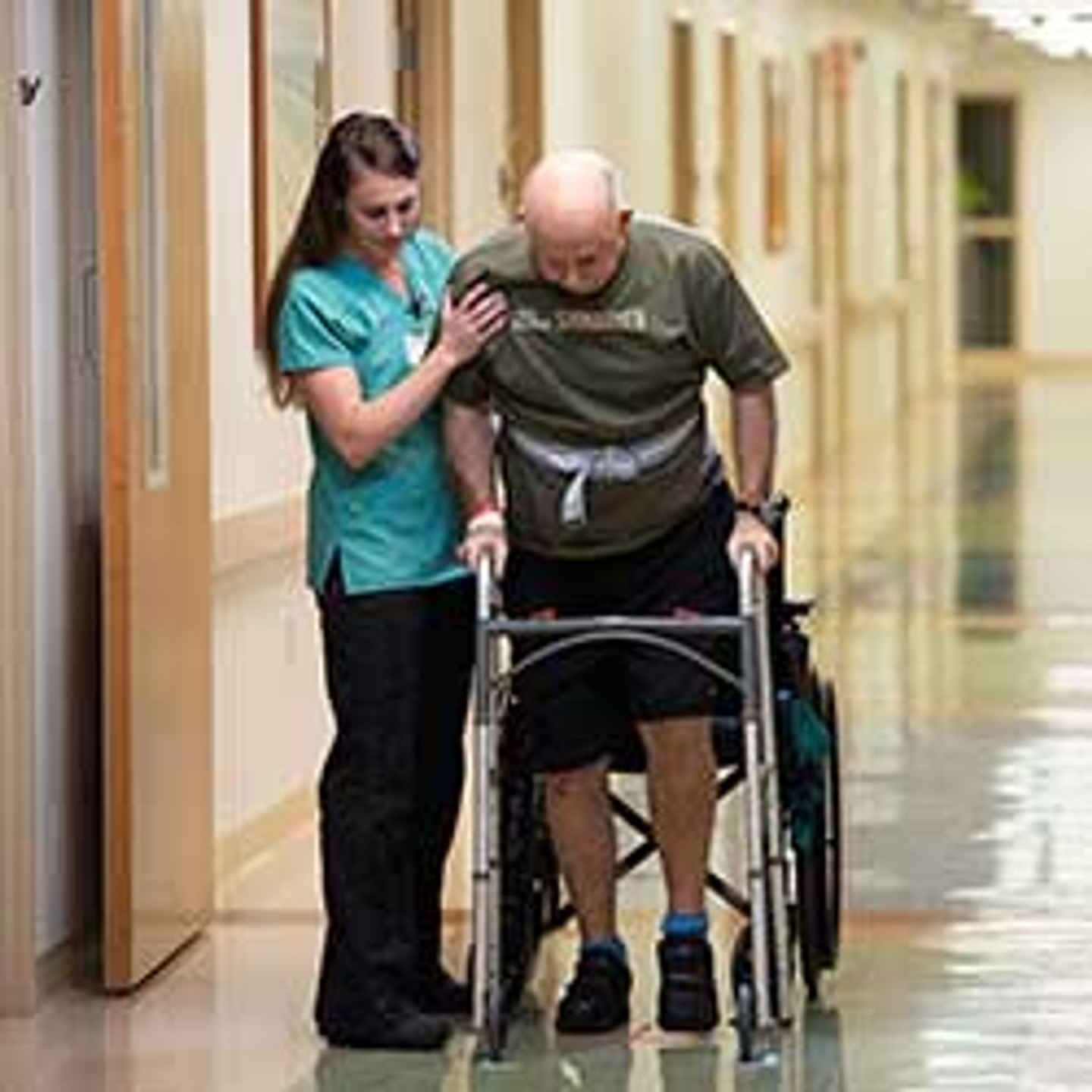 Physical therapist helping a patient walk down a hallway.