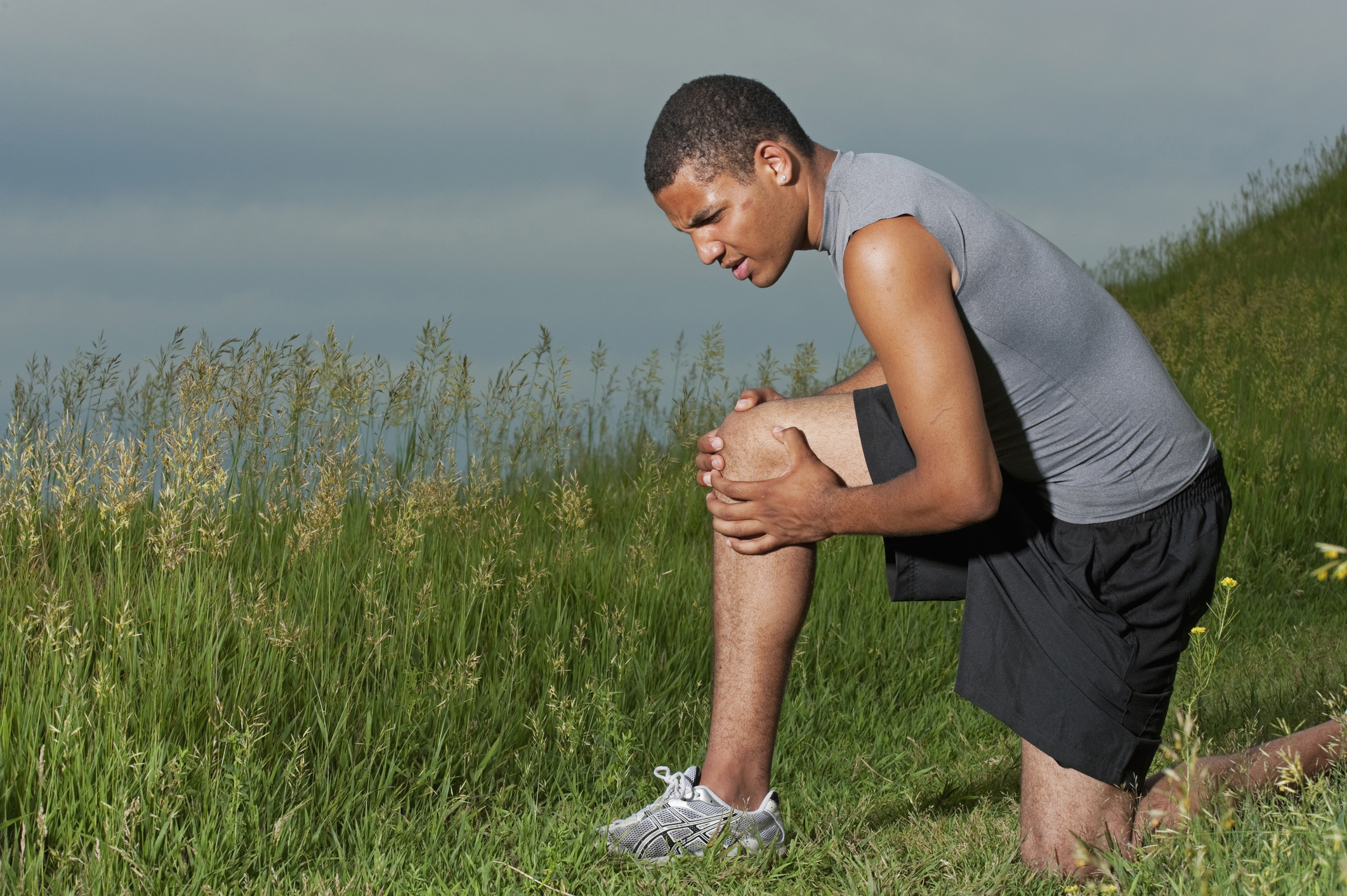 A runner kneeling and grabbing one knee in the middle of a field