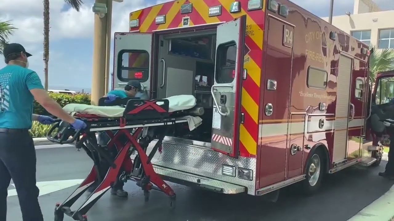 Two EMTs wheel an empty stretcher into the back of an ambulance