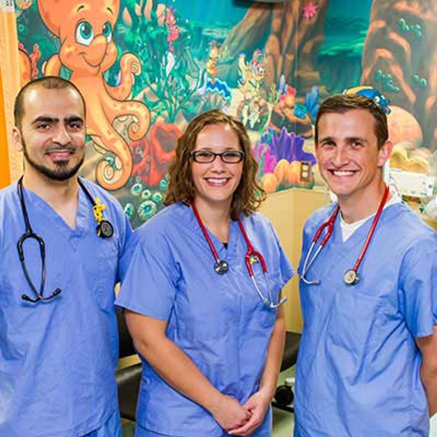 Three staff members of Gulf Coast Hospital posing in front of an ocean-themed mural.