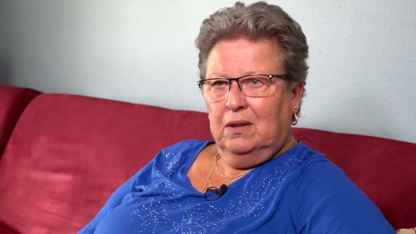 Helen Horty  sits on a red sofa and addresses on off screen interviewer