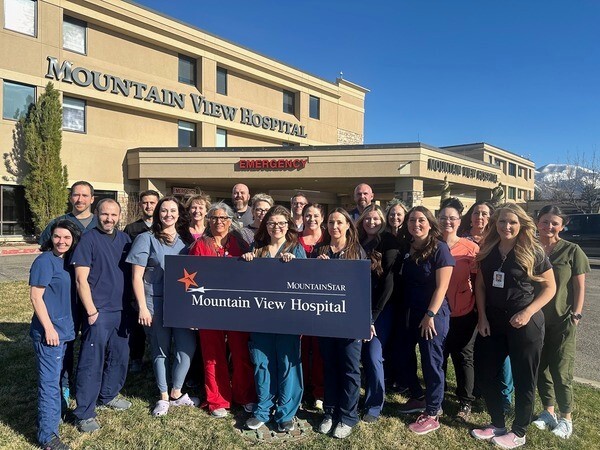 Colleagues who work in HCA Healthcare/MountainStar Healthcare's Mountain View Hospital ICU smile and pose together outside the Payson, Utah facility after being awarded a Unit of Distinction. They're holding a sign that reads "Mountain View Hospital."