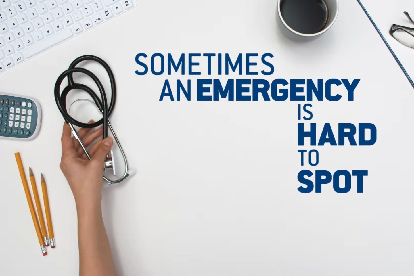 A person's hand reaches across a work desk holding a stethoscope, along with the text, "Sometimes an emergency is hard to spot."