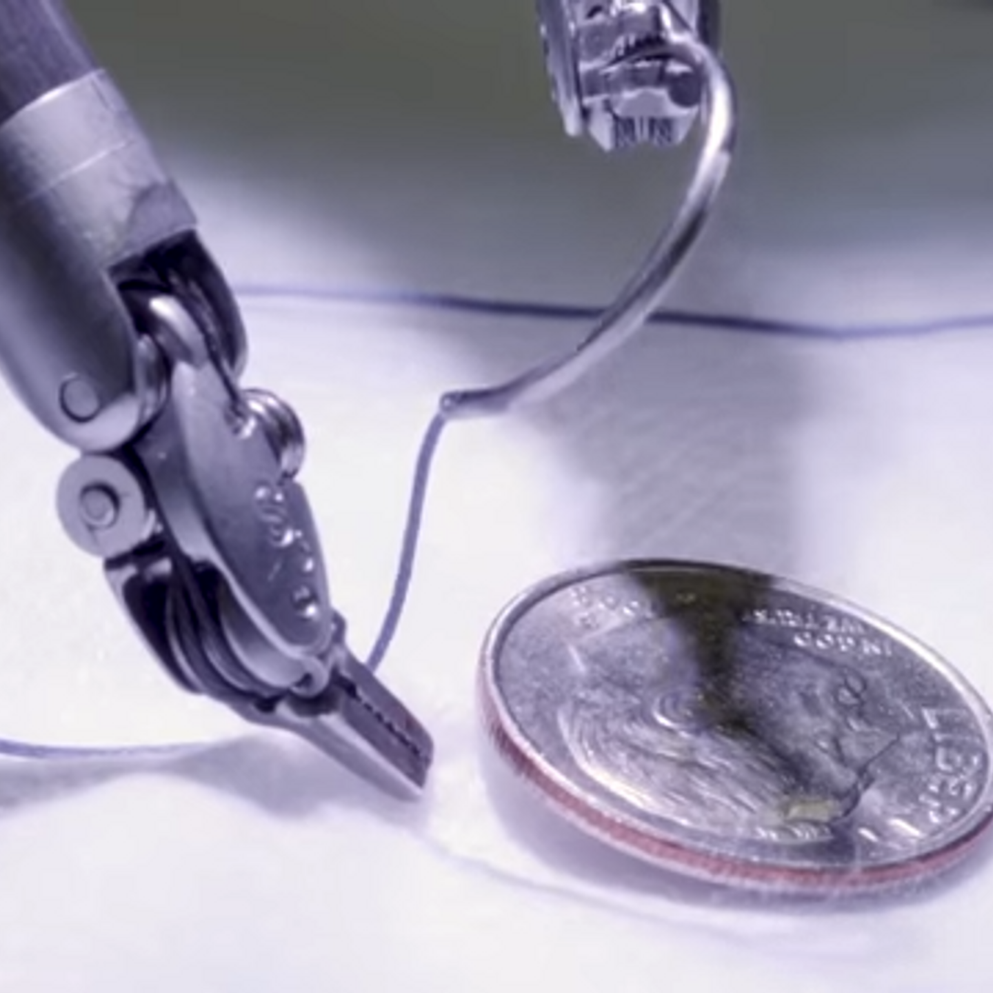 A robotic device sows thread through cloth. A dime is pictured for scale.