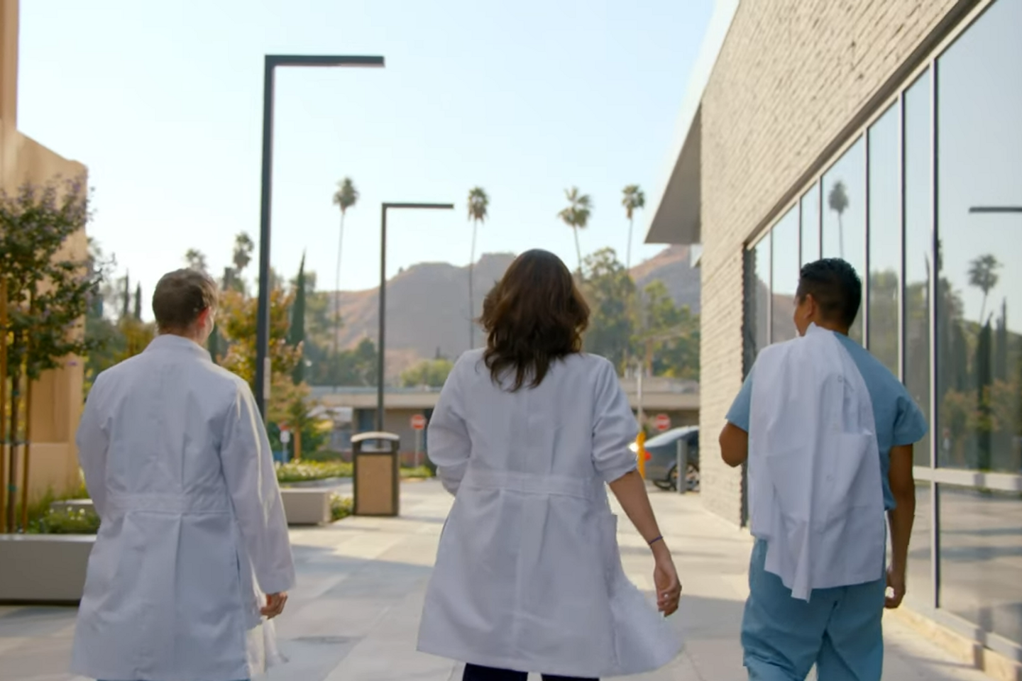 Three graduate medical students walk together in a breezeway between two buildings.