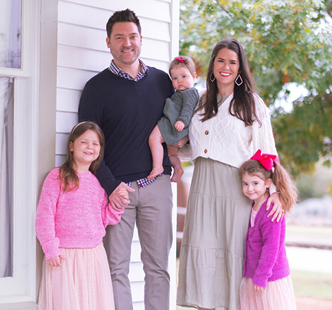 Karen Adams smiles while standing on the porch with her husband and three daughters.