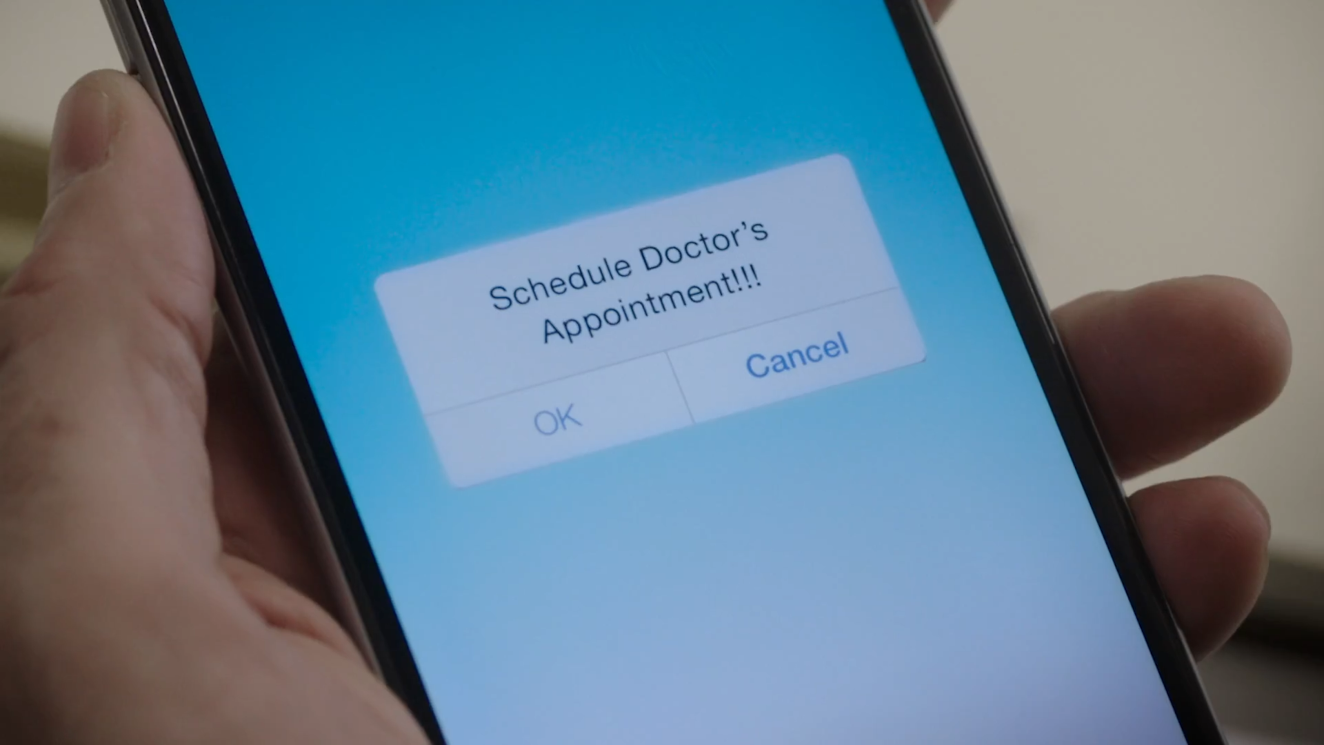 A closeup of a left hand holding a cell phone screen that displays a  "Schedule Doctor's Appointment!!!" notification.