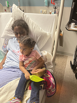 Ramoni smiles while sitting in a hospital bed with her daughter.