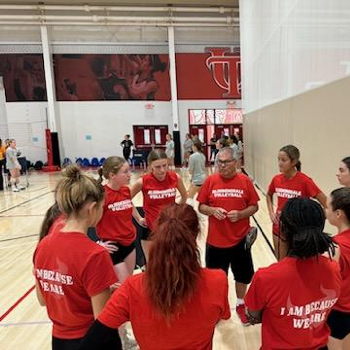 Coach Tim and his team huddles on the volleyball court.